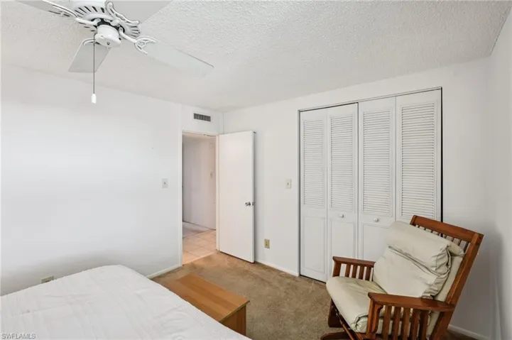 Bedroom with a textured ceiling, light colored carpet, ceiling fan, and a closet