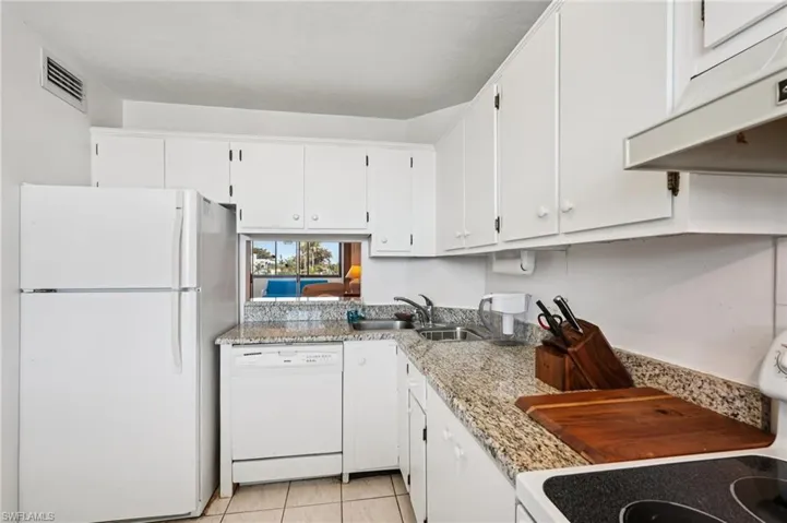 Kitchen with white appliances, white cabinetry, light stone counters, and light tile patterned floors