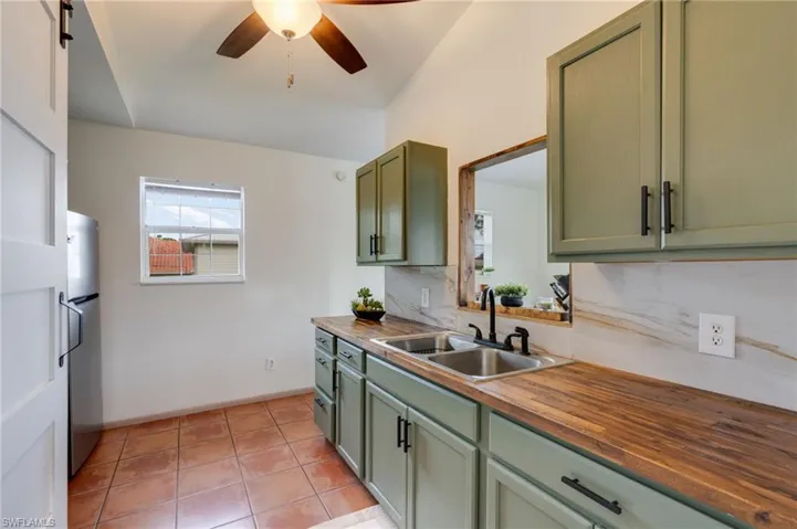 Kitchen featuring a vaulted ceiling with a ceiling fan, terracotta tile flooring, green cabinetry with black hardware, wood-finish countertops, and a stainless steel double sink with a black faucet