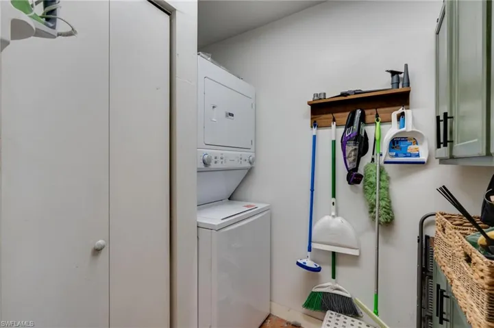 Dedicated laundry area featuring a white stacked washer and dryer, integrated shelving, and white cabinetry with dark pulls