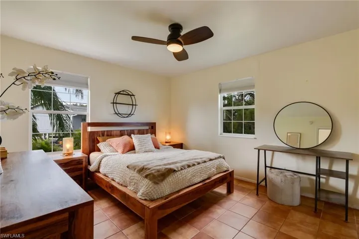 Bedroom featuring terra cotta tile flooring, a ceiling fan with integrated lighting, and multiple windows with white frames