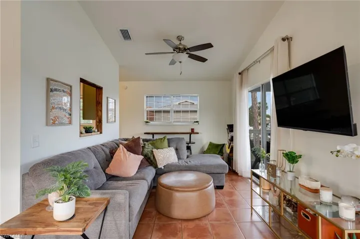 Living area featuring vaulted ceilings, terra cotta style tile flooring, a ceiling fan, and sliding glass door access to an outdoor space