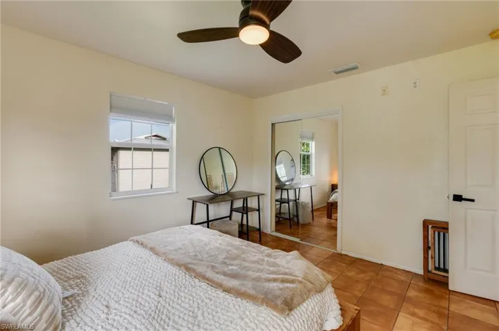 Interior room featuring neutral wall tones, tile flooring, a window with a white frame, a ceiling fan with integrated lighting, and a mirrored sliding closet door