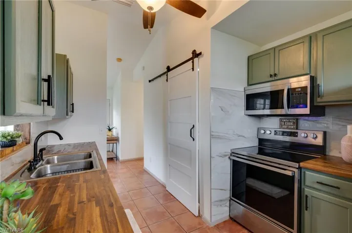 Kitchen featuring wood-finish countertops, a double basin stainless steel sink with a matte black faucet, and sage green cabinetry