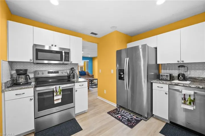 Kitchen with tasteful backsplash, dark stone countertops, white cabinetry, and stainless steel appliances