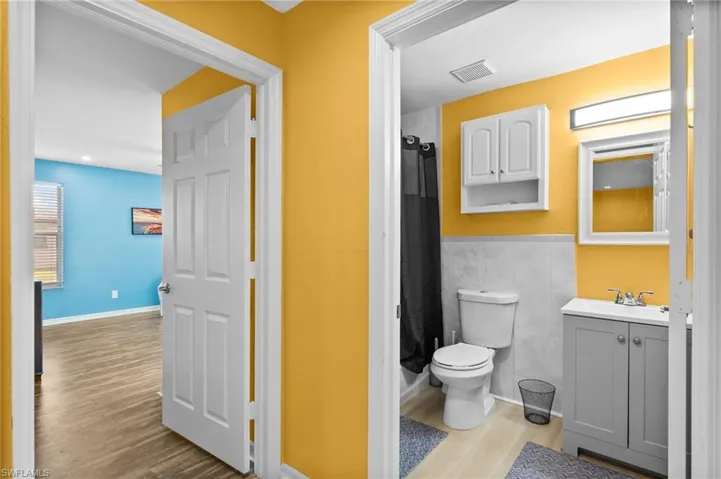 Bathroom featuring vanity, a shower with curtain, toilet, tile walls, and wood-type flooring