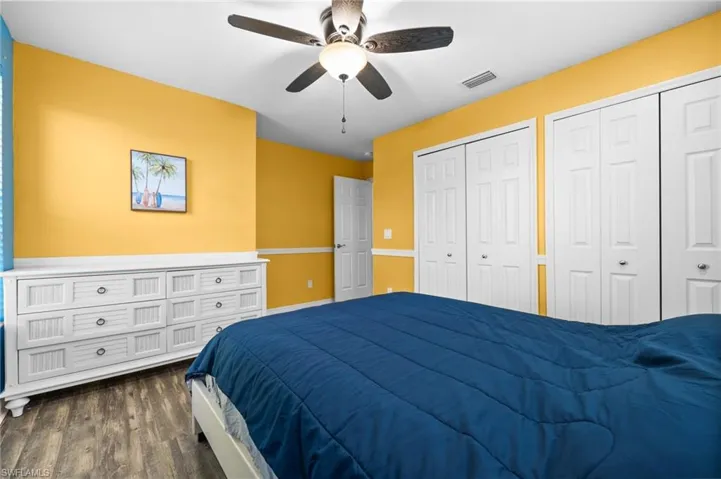 Bedroom with ceiling fan, dark hardwood / wood-style floors, and multiple closets