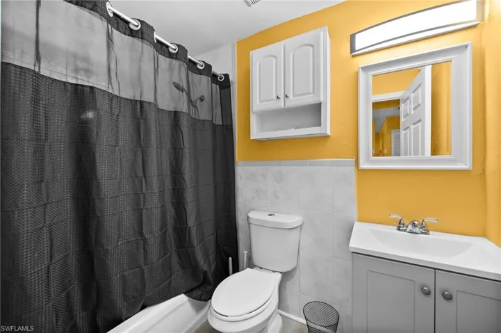 Full bathroom featuring shower / bath combination with curtain, vanity, toilet, and tile walls