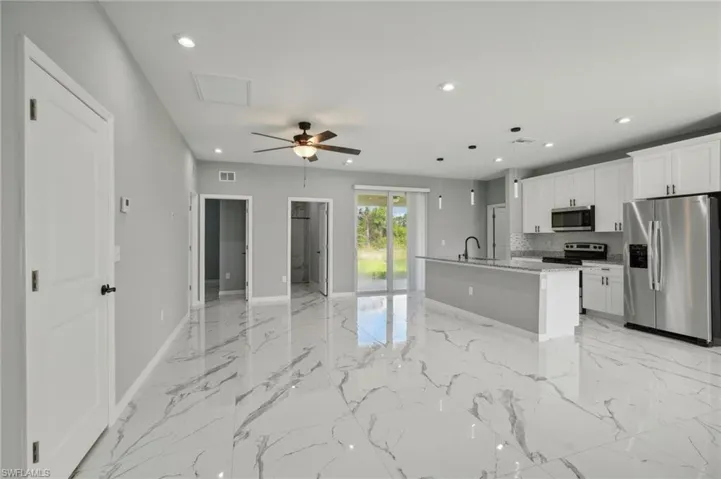 Kitchen featuring stainless steel appliances, light tile patterned floors, a kitchen island with sink, white cabinets, and ceiling fan