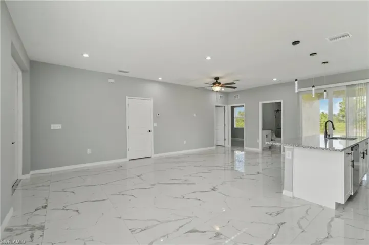 Kitchen featuring a center island with sink, light tile patterned floors, white cabinetry, ceiling fan, and decorative light fixtures