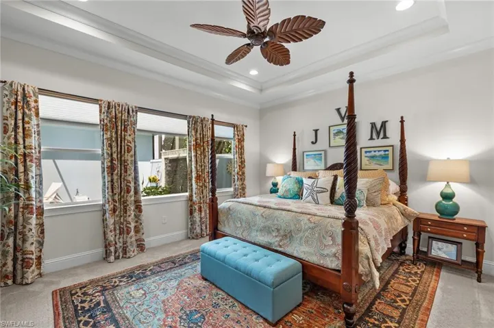 Bedroom with carpet, a tray ceiling, ceiling fan, and multiple windows