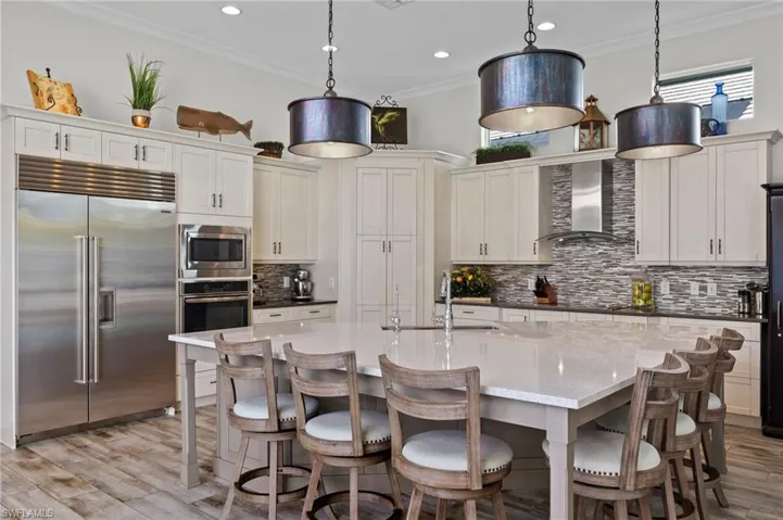 Kitchen featuring built in appliances, backsplash, wall chimney range hood, and decorative light fixtures
