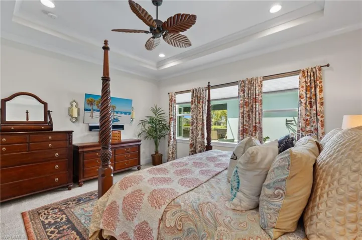 Carpeted bedroom featuring ceiling fan, crown molding, and a raised ceiling