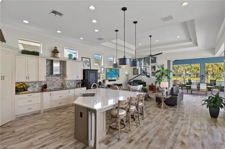 Kitchen with a raised ceiling, gas stovetop, wall chimney exhaust hood, a center island with sink, and sink
