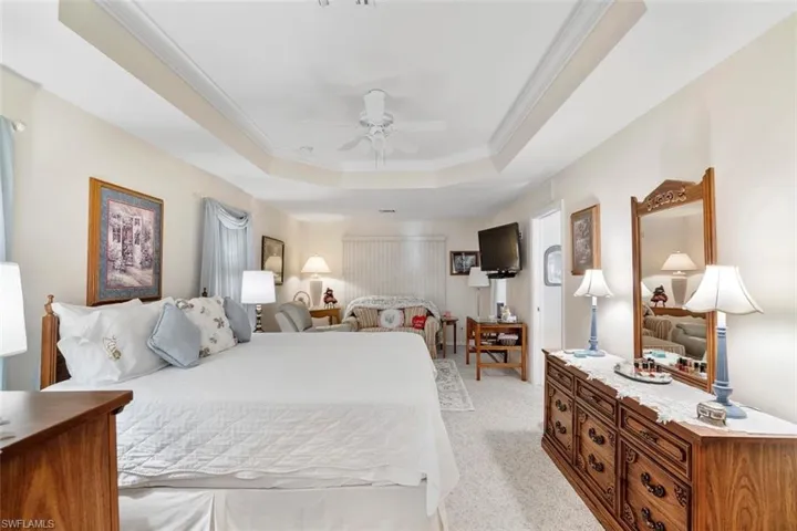 Bedroom featuring a tray ceiling, ceiling fan, crown molding, and light carpet