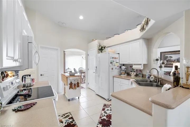 Kitchen with white cabinetry, sink, light tile patterned floors, stove, and white refrigerator with ice dispenser