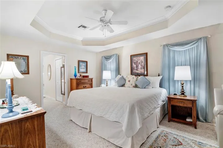 Bedroom featuring ceiling fan, a raised ceiling, crown molding, and light colored carpet