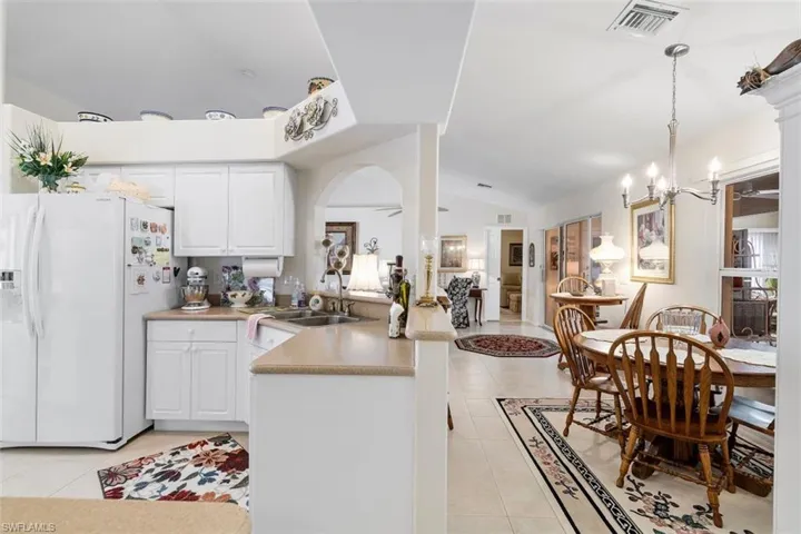 Kitchen featuring light tile patterned flooring, vaulted ceiling, sink, and white fridge with ice dispenser