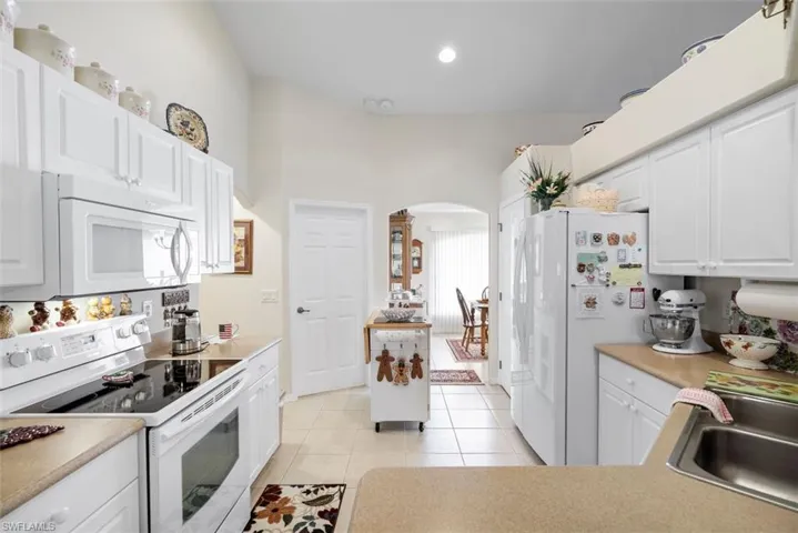 Kitchen featuring sink, white appliances, light tile patterned flooring, and white cabinets