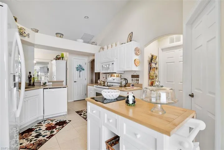 Kitchen with white appliances, white cabinets, light tile patterned floors, and wooden counters