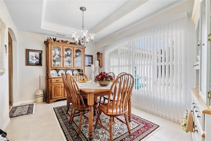 Dining area with a tray ceiling, light tile patterned flooring, and a chandelier