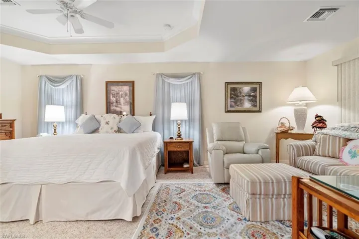 Bedroom featuring ceiling fan, a raised ceiling, ornamental molding, and light colored carpet