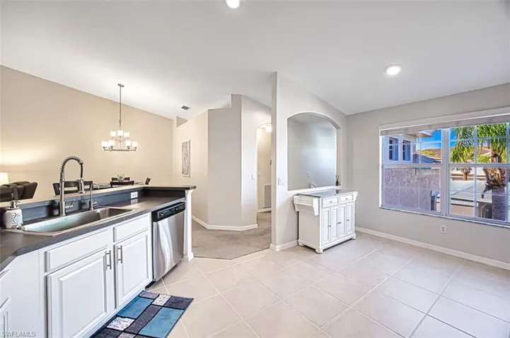 Kitchen featuring dishwasher, sink, a chandelier, lofted ceiling, and white cabinets
