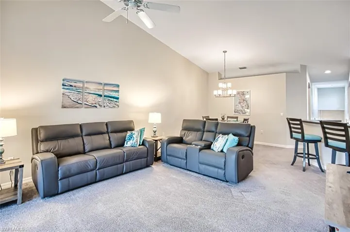 Living room with carpet flooring, ceiling fan with notable chandelier, and lofted ceiling