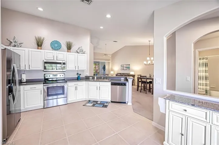 Kitchen with appliances with stainless steel finishes, sink, light tile patterned floors, decorative light fixtures, and white cabinetry