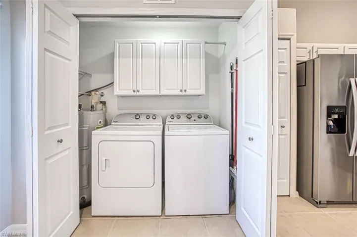 Laundry area featuring washer and clothes dryer, light tile patterned floors, and cabinets
