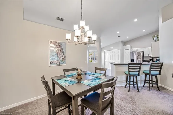Carpeted dining area with vaulted ceiling and a notable chandelier