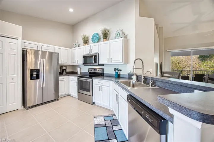 Kitchen with sink, light tile patterned floors, appliances with stainless steel finishes, white cabinetry, and kitchen peninsula