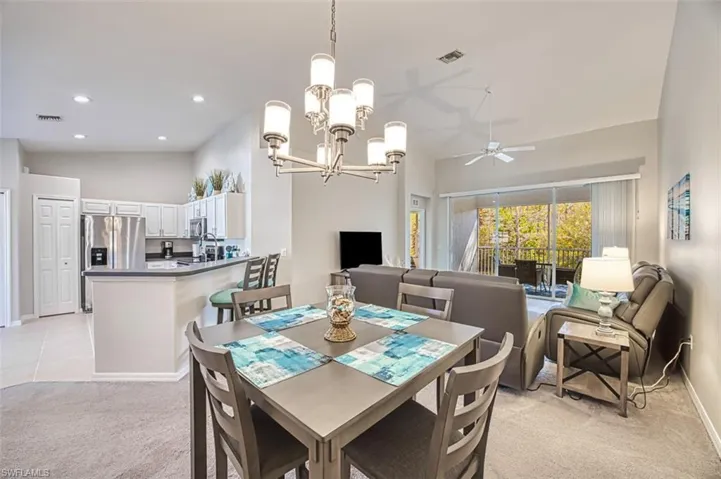 Dining space featuring vaulted ceiling, light colored carpet, and ceiling fan with notable chandelier