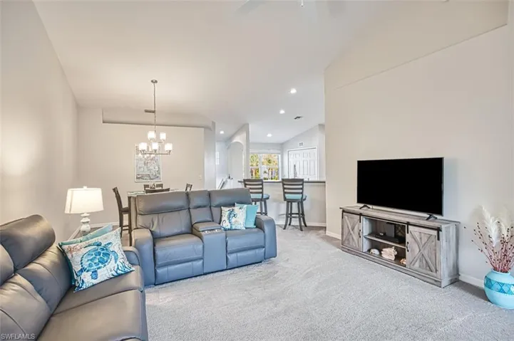 Living room featuring vaulted ceiling, light colored carpet, and an inviting chandelier