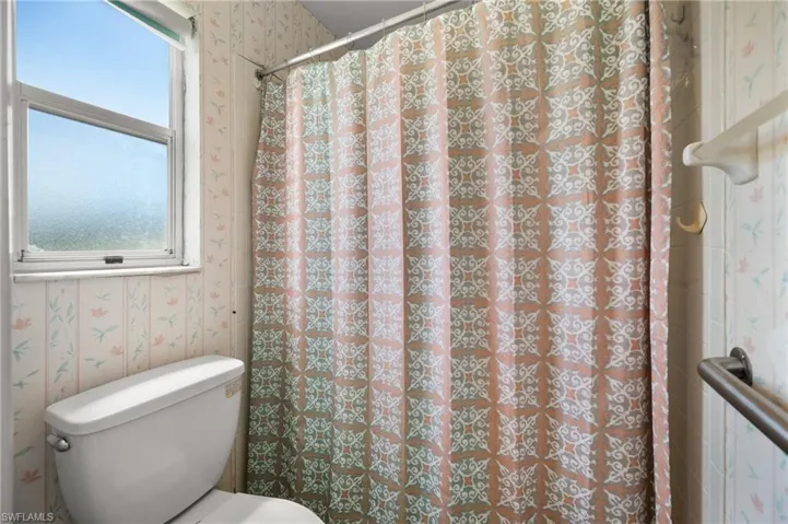 Toilet with a window, grab bar, and patterned wall covering