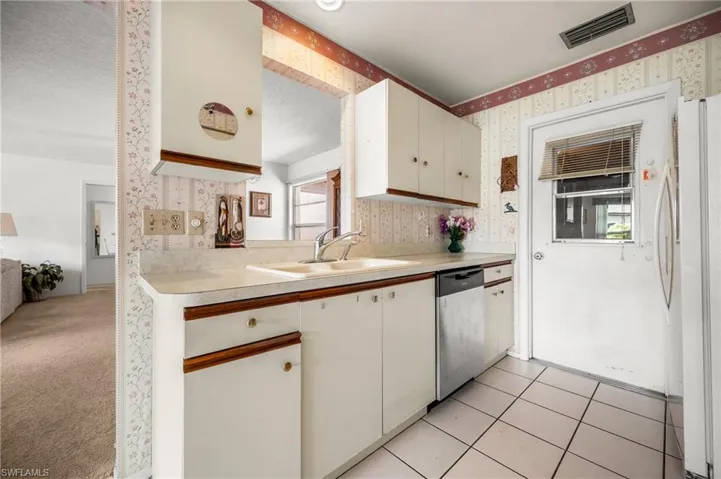 White cabinetry with wood-finish accents, dual basin sink, white countertops, and white tile flooring