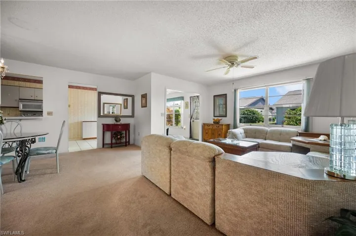 Expansive living area with large windows, a ceiling fan, and carpeted flooring