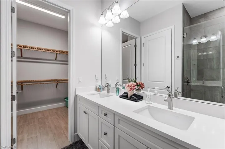 Bathroom with double vanity, light wood-style flooring, a stall shower, and a spacious closet