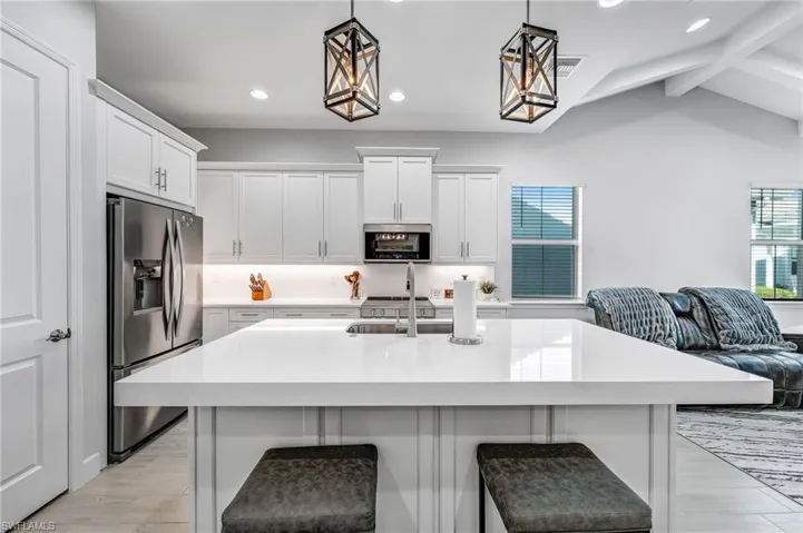Kitchen featuring appliances with stainless steel finishes, white cabinets, a kitchen island with sink, decorative light fixtures, and a kitchen breakfast bar