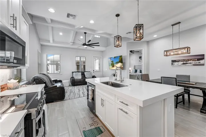 Kitchen featuring white cabinetry, ceiling fan, open floor plan, decorative light fixtures, and beamed ceiling