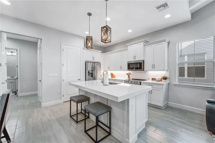 Kitchen with a breakfast bar area, a center island with sink, decorative light fixtures, white cabinetry, and stainless steel appliances