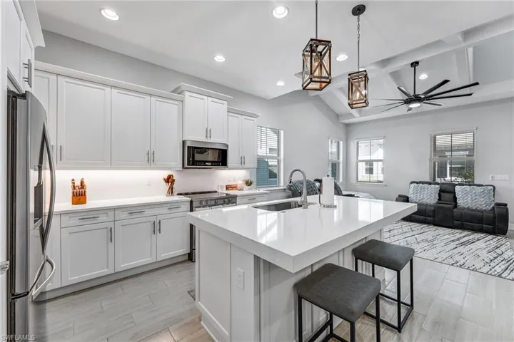 Kitchen featuring a center island with sink, open floor plan, pendant lighting, white cabinetry, and beamed ceiling