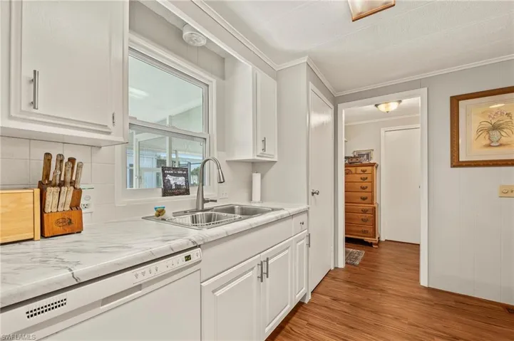 Kitchen featuring dishwasher, sink, light hardwood / wood-style flooring, white cabinets, and ornamental molding
