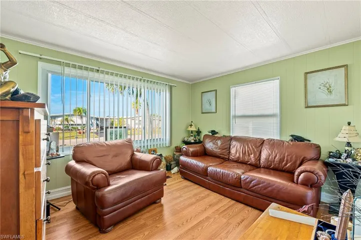 Living room with ornamental molding, a textured ceiling, and light wood-type flooring