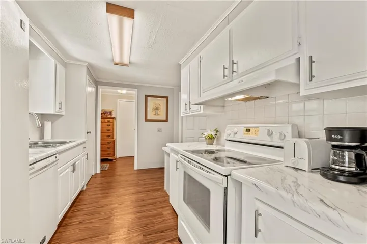 Kitchen with sink, white appliances, decorative backsplash, white cabinets, and custom range hood