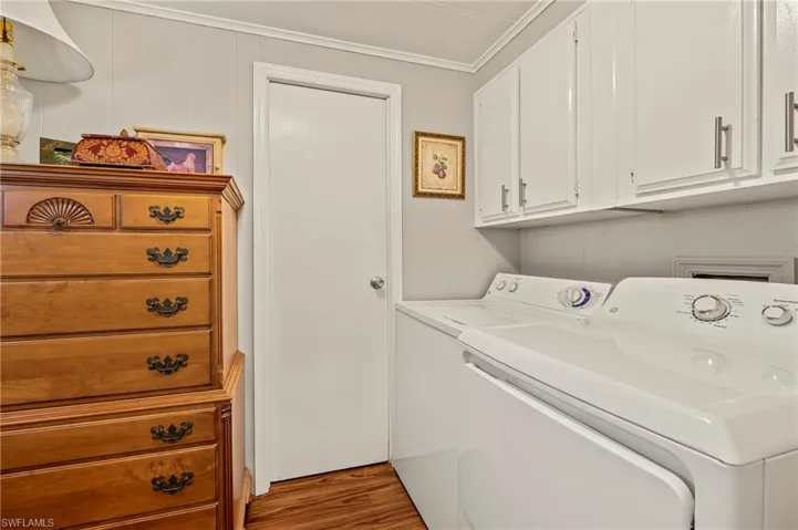 Clothes washing area with washer and clothes dryer, cabinets, ornamental molding, and light wood-type flooring