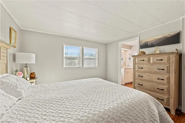 Bedroom with connected bathroom, wood walls, dark wood-type flooring, and a textured ceiling