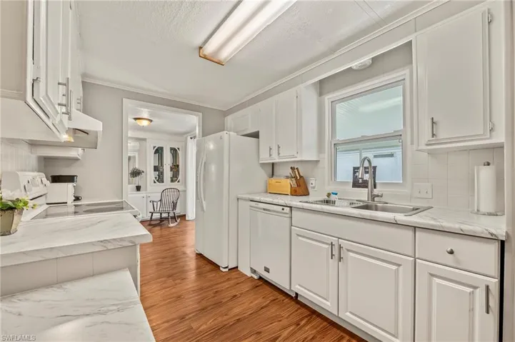 Kitchen with white cabinetry, sink, crown molding, hardwood / wood-style floors, and white appliances