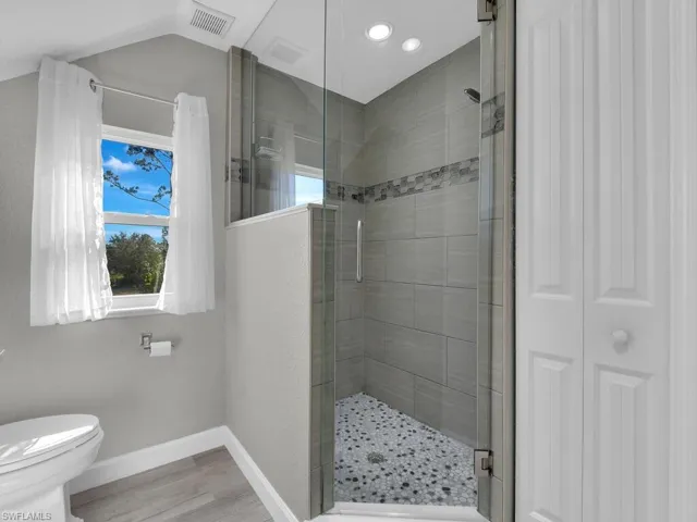 Full bath with a shower stall, a closet, and light wood-style floors