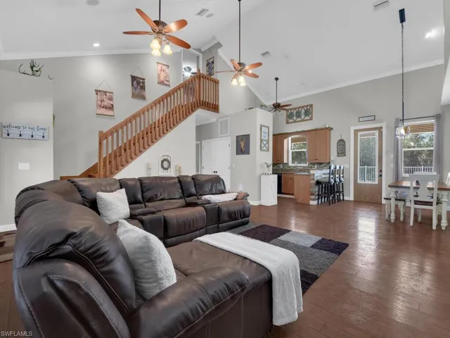 Living area featuring crown molding, high vaulted ceiling, a ceiling fan, and dark wood-style floors